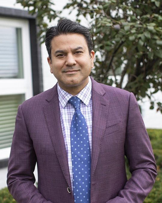 Portrait of Dr. Ahmed from the waist up. Man with purple suit, blue tie, and black hair.