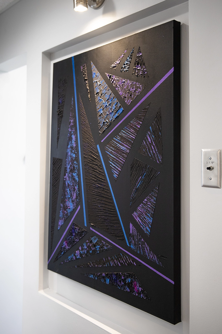 Abstract art piece of a black background with textured triangles in shades of blue to purple.