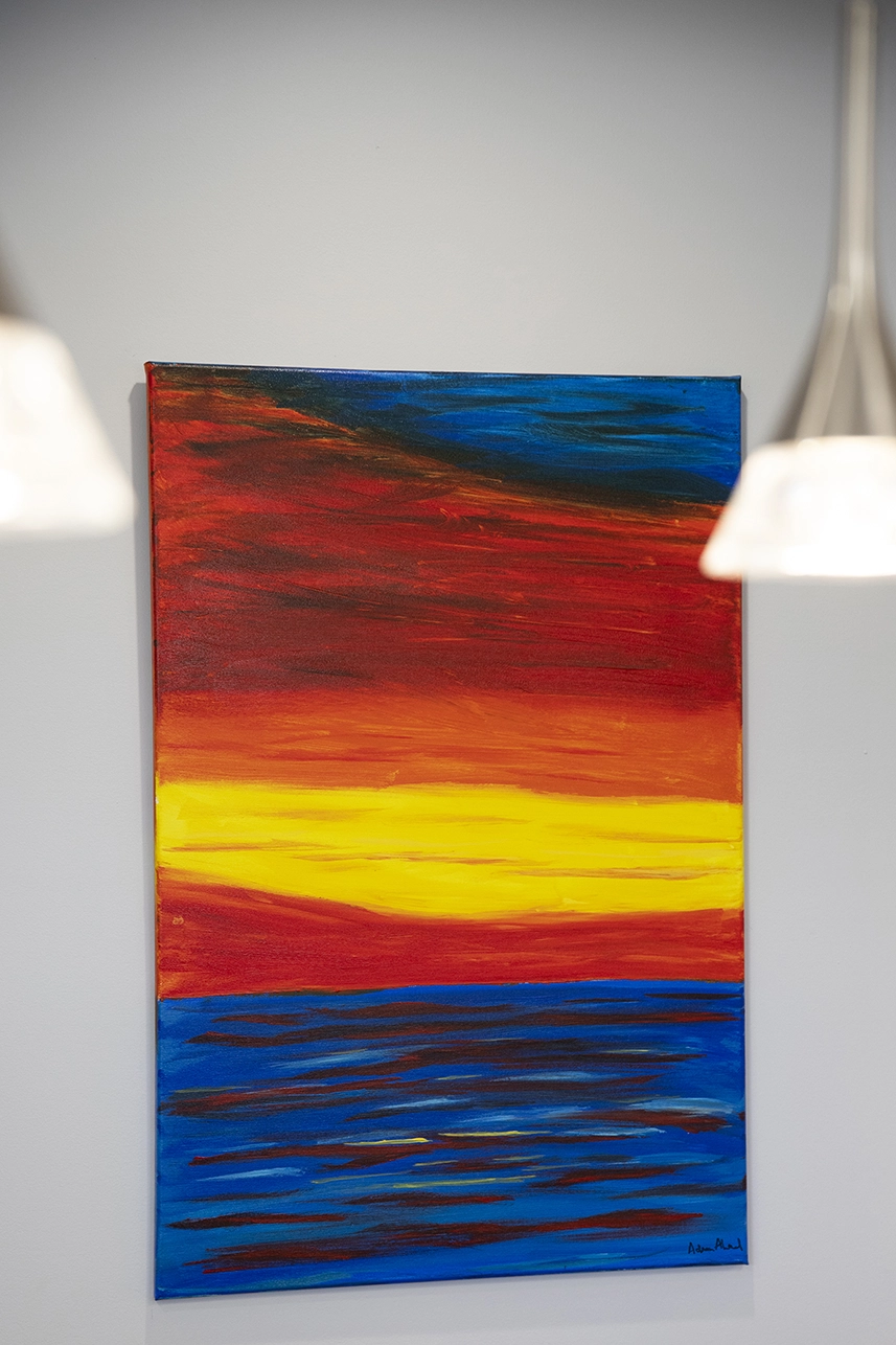 Abstract art piece of the sunset over the ocean. The ocean is blue and the sunset is red, yellow, orange, and blue.