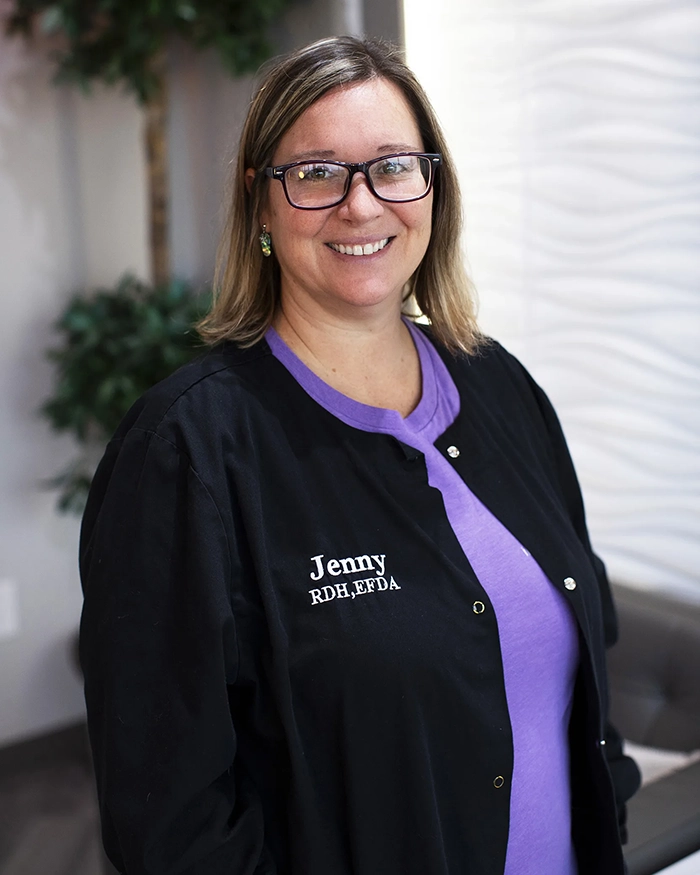 Portrait of Jennifer, Dental Assistant from the waist up. Woman in black uniform and purple shirt.
