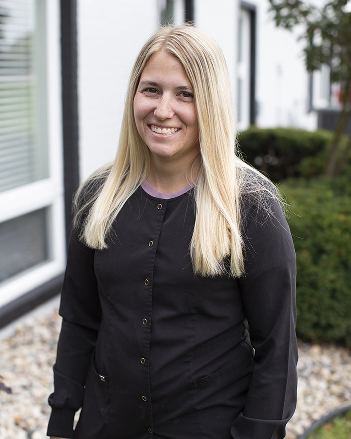 Portrait of Kara, Dental Assistant from the waist up. Woman in black uniform with blonde hair.