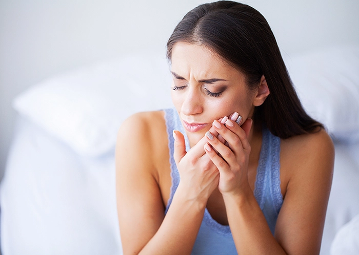 Brunette woman grimacing while holding her hands over her jaw.