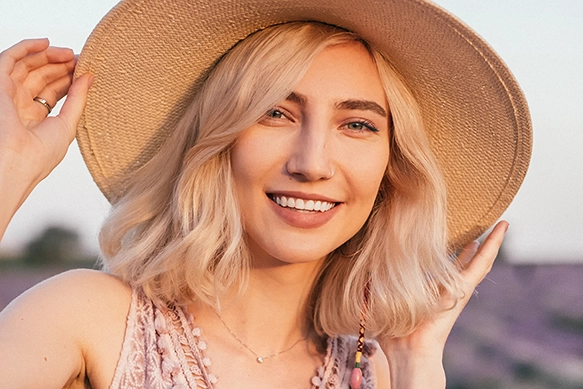 Blonde woman smiling, wearing a sun hat.