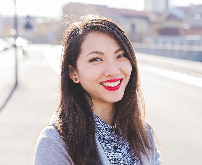 Brunette woman standing outside smiling while wearing bright red lipstick